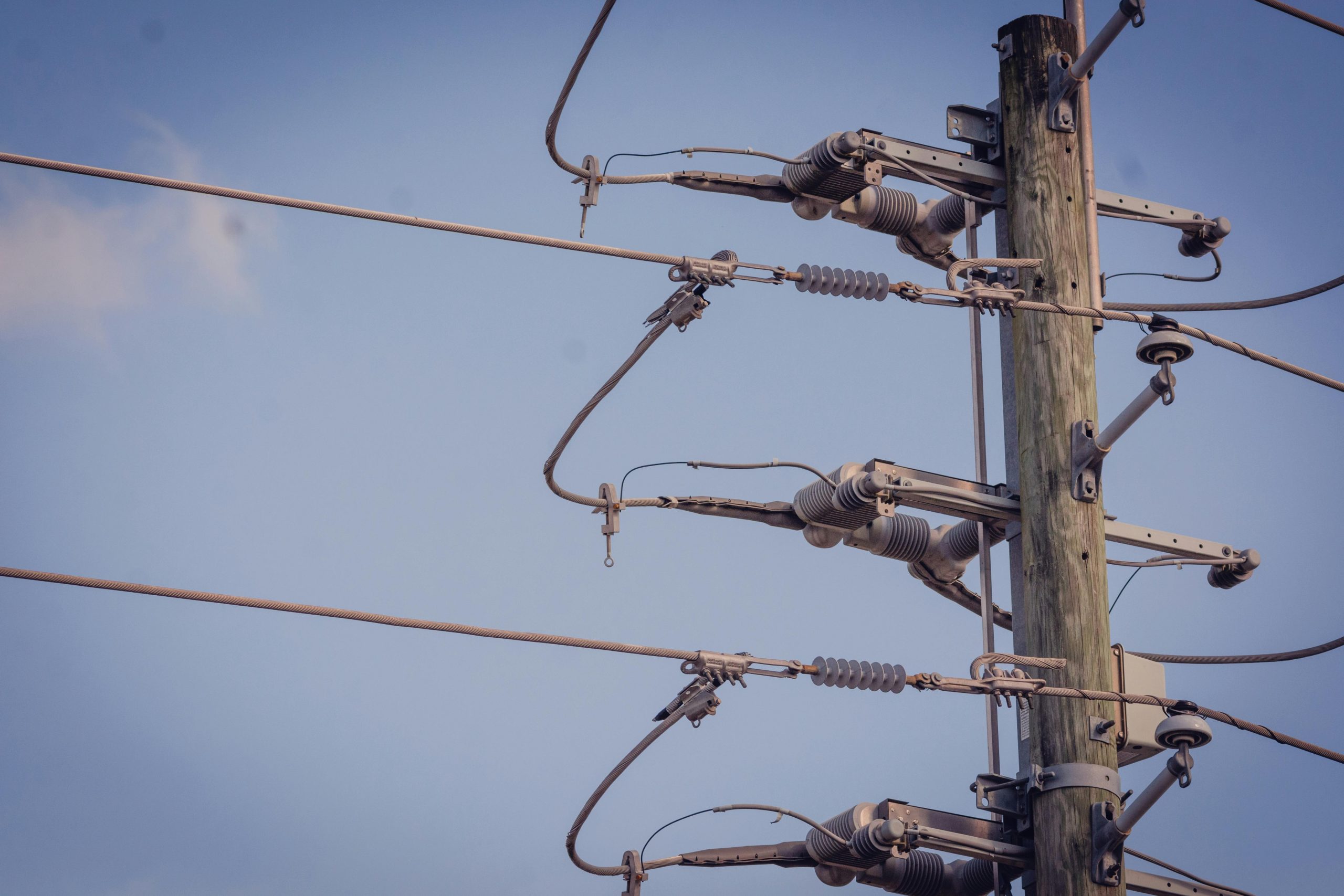 Detailed view of a power pole and lines against a clear blue sky.
