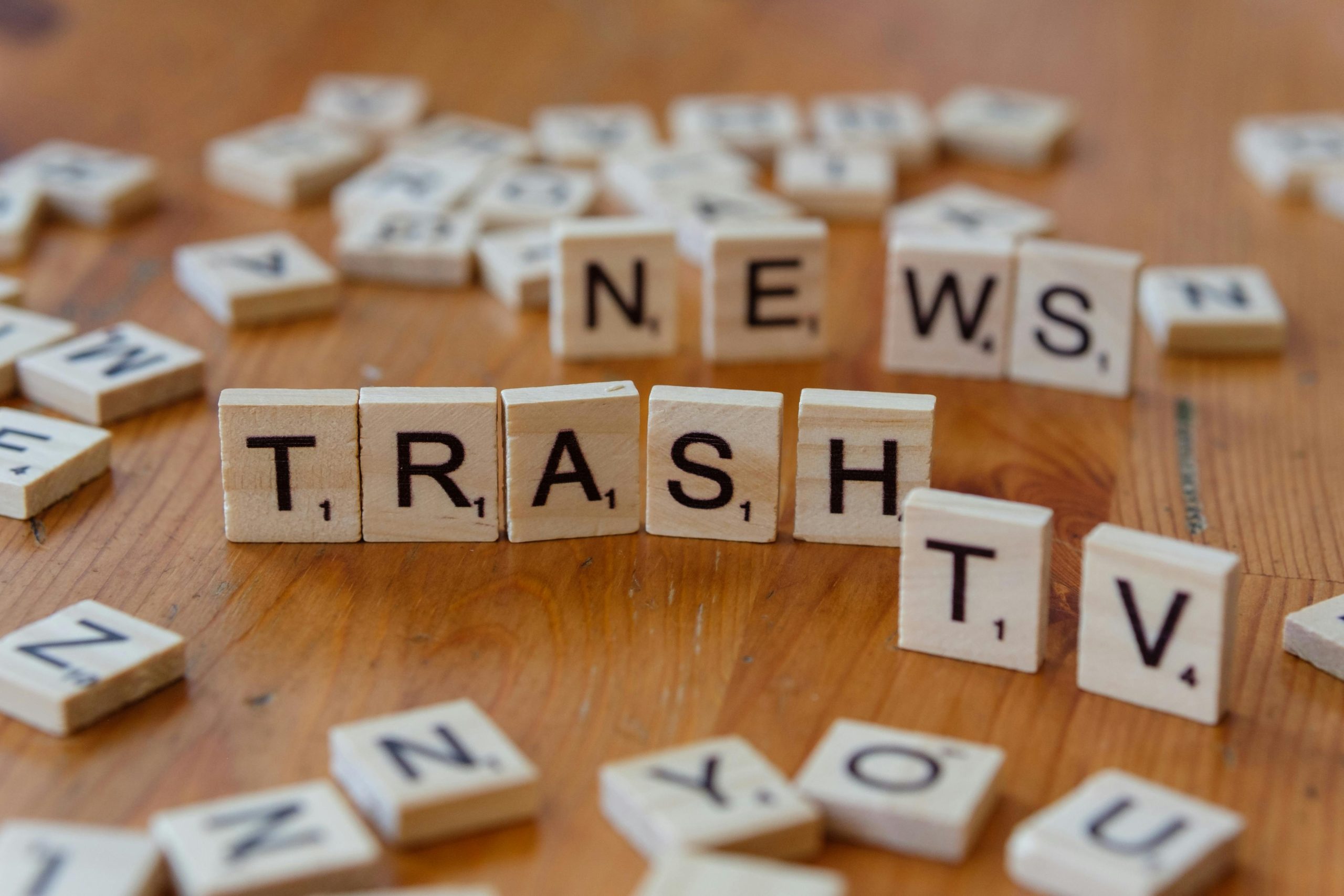 Close-up of wooden letter tiles spelling out Trash TV News on a table.