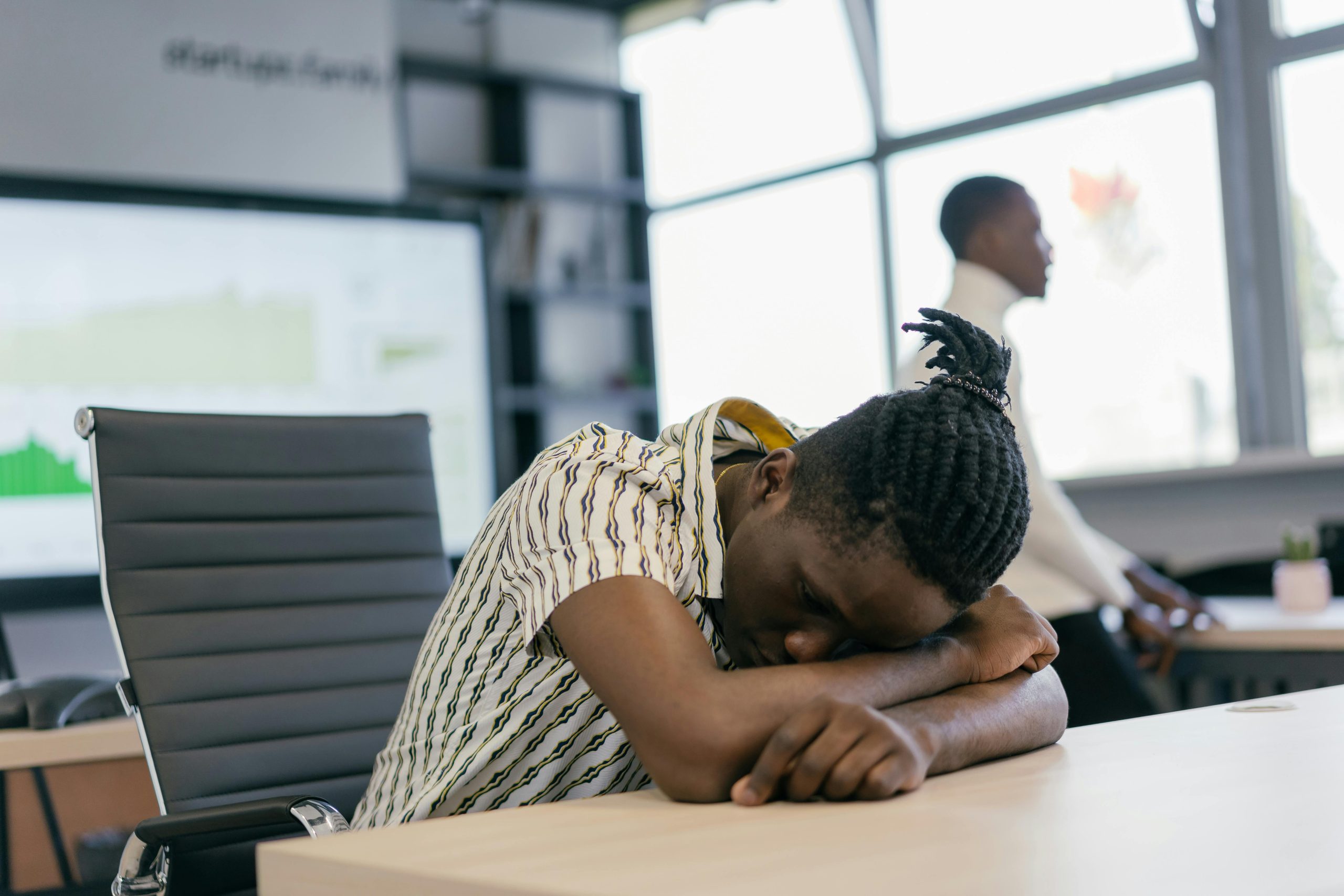 An office worker rests with head on desk, conveying fatigue in a modern workspace.